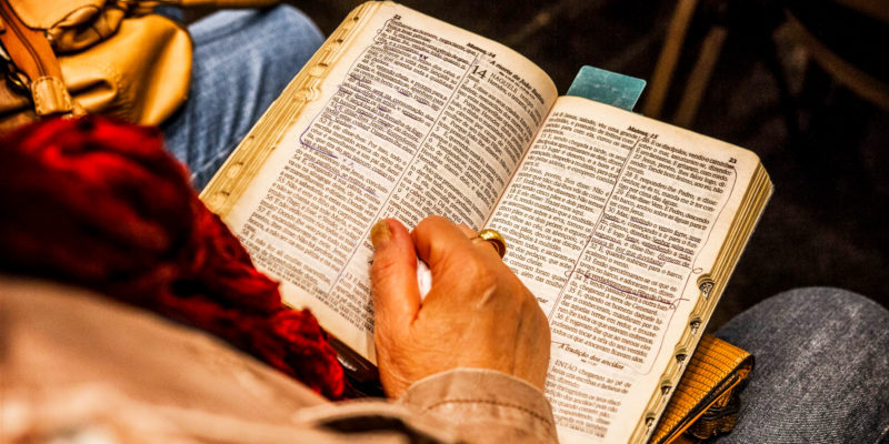 Older persons hands, holding a tissue on an open bible in their lap.