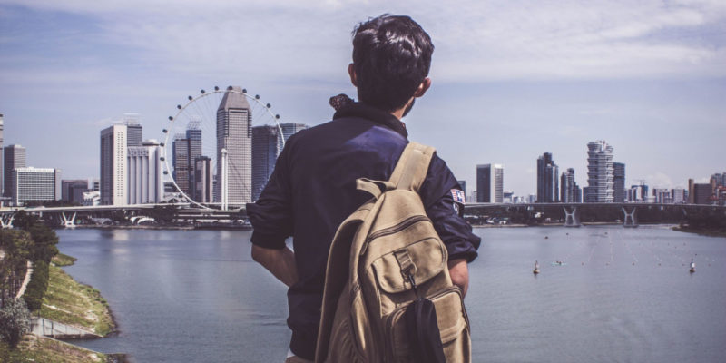 Cover photo for "Let's Slow Down: Framing the COVID-19 Pandemic as a Sabbath event". A man with a backpack looking at Singapore Harbor.